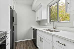 Kitchen with white cabinets, dark wood-type flooring, appliances with stainless steel finishes, and light stone counters