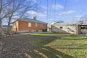 Back of house featuring a patio, a yard, a chimney, brick siding, and an outbuilding