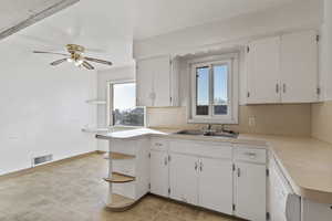 Kitchen with light countertops, open shelves, a peninsula, white cabinets, and white dishwasher