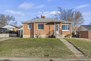 Bungalow featuring brick siding, a front yard, a shingled roof, and a chimney