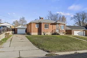 View of front of property with an outdoor structure, a front lawn, brick siding, concrete driveway, and a detached garage