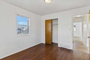 Unfurnished bedroom featuring dark wood-style floors, multiple windows, and a closet