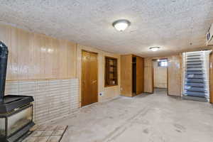 Below grade area featuring wooden walls, a wood stove, and stairs