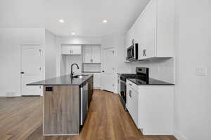 Kitchen with white cabinetry, appliances with stainless steel finishes, a center island with sink, backsplash, and dark stone counters