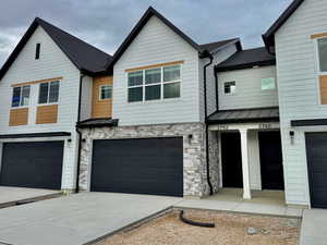 View of front of property featuring a standing seam roof, a metal roof, stone siding, an attached garage, and driveway