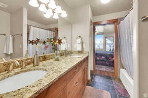Ensuite bathroom featuring double vanity, shower / bath combo with shower curtain, and stone tile flooring