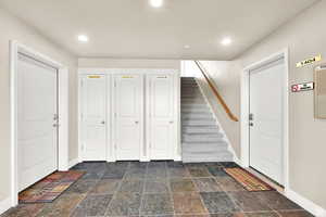 Foyer entrance with stone tile floors, stairs, and recessed lighting