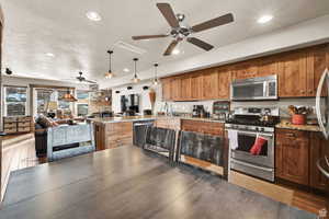 Kitchen featuring light stone counters, ceiling fan, appliances with stainless steel finishes, a peninsula, and hanging light fixtures