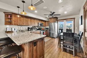 Kitchen featuring light stone countertops, stainless steel appliances, a peninsula, decorative light fixtures, and a breakfast bar area