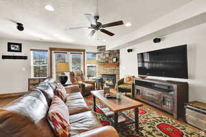 Living room with a textured ceiling, a stone fireplace, ceiling fan, recessed lighting, and wood finished floors