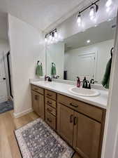 Full bathroom featuring double vanity, light wood finished floors, a stall shower, and a textured ceiling