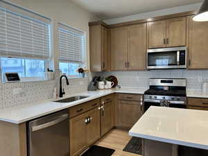 Kitchen with light stone countertops, stainless steel appliances, decorative backsplash, and brown cabinets