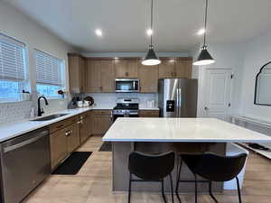 Kitchen featuring stainless steel appliances, decorative light fixtures, light wood-style flooring, and backsplash