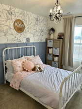 Carpeted bedroom with a chandelier, a textured ceiling, and wallpapered walls
