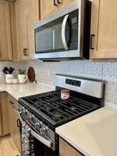 Kitchen with appliances with stainless steel finishes, decorative backsplash, light stone countertops, and light wood finished floors