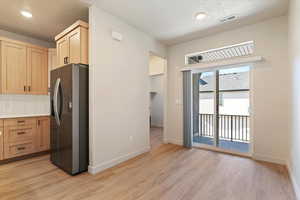 Kitchen featuring stainless steel fridge with ice dispenser, decorative backsplash, light wood-type flooring, light countertops, and a textured ceiling