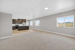 Kitchen with dark brown cabinets, light countertops, open floor plan, stainless steel appliances, and a center island with sink