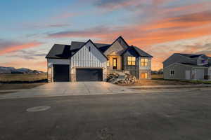 Modern farmhouse style home featuring board and batten siding, a garage, driveway, and stone siding