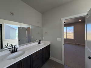 Bathroom featuring double vanity, dark colored carpet, and dark tile patterned floors