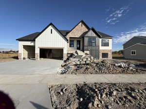View of front of property with board and batten siding, concrete driveway, and brick siding