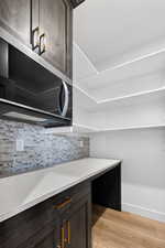 Bar with dark brown cabinets, stainless steel microwave, light wood-type flooring, and light stone countertops