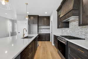 Kitchen with dark brown cabinets, stainless steel appliances, light stone counters, light wood-type flooring, and pendant lighting