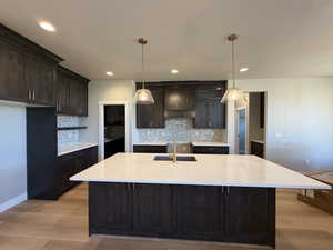 Kitchen featuring light stone countertops, backsplash, dark brown cabinetry, light wood-style flooring, and recessed lighting