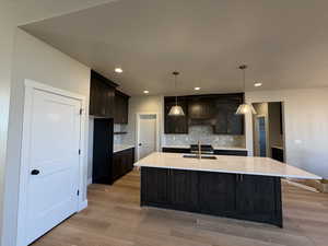 Kitchen featuring light stone countertops, backsplash, a center island with sink, light wood-type flooring, and recessed lighting