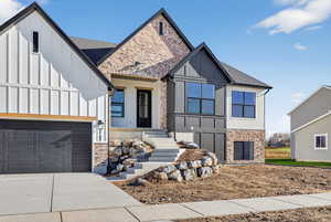 View of front facade with board and batten siding, driveway, an attached garage, and roof with shingles