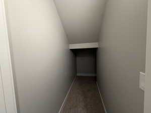 Hallway with a textured ceiling, vaulted ceiling, and light carpet