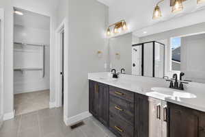 Full bathroom with a spacious closet, a shower stall, double vanity, and light tile patterned flooring