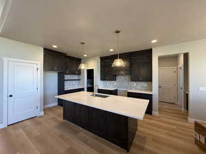 Kitchen featuring dark brown cabinets, light stone countertops, backsplash, a kitchen island with sink, and recessed lighting