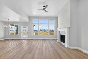Unfurnished living room featuring light wood-style flooring, a fireplace, a ceiling fan, a chandelier, and plenty of natural light