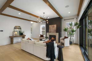 Living room with a large fireplace, beam ceiling, light wood-style floors, a chandelier, and recessed lighting