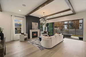 Living area with beam ceiling, a fireplace, a chandelier, light wood-style flooring, and plenty of natural light