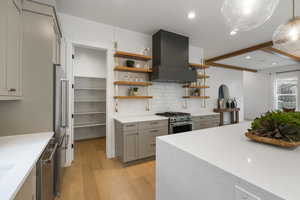 Kitchen with gray cabinetry, light stone counters, light wood-style floors, backsplash, and range hood