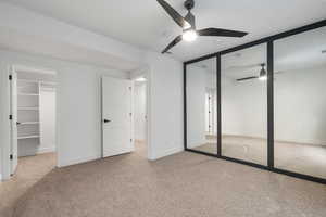 Unfurnished bedroom featuring light carpet, a spacious closet, and a ceiling fan