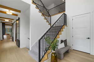 Stairs featuring wood finished floors, a barn door, beamed ceiling, a high ceiling, and recessed lighting
