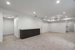 Below grade area featuring light carpet, recessed lighting, and a chandelier