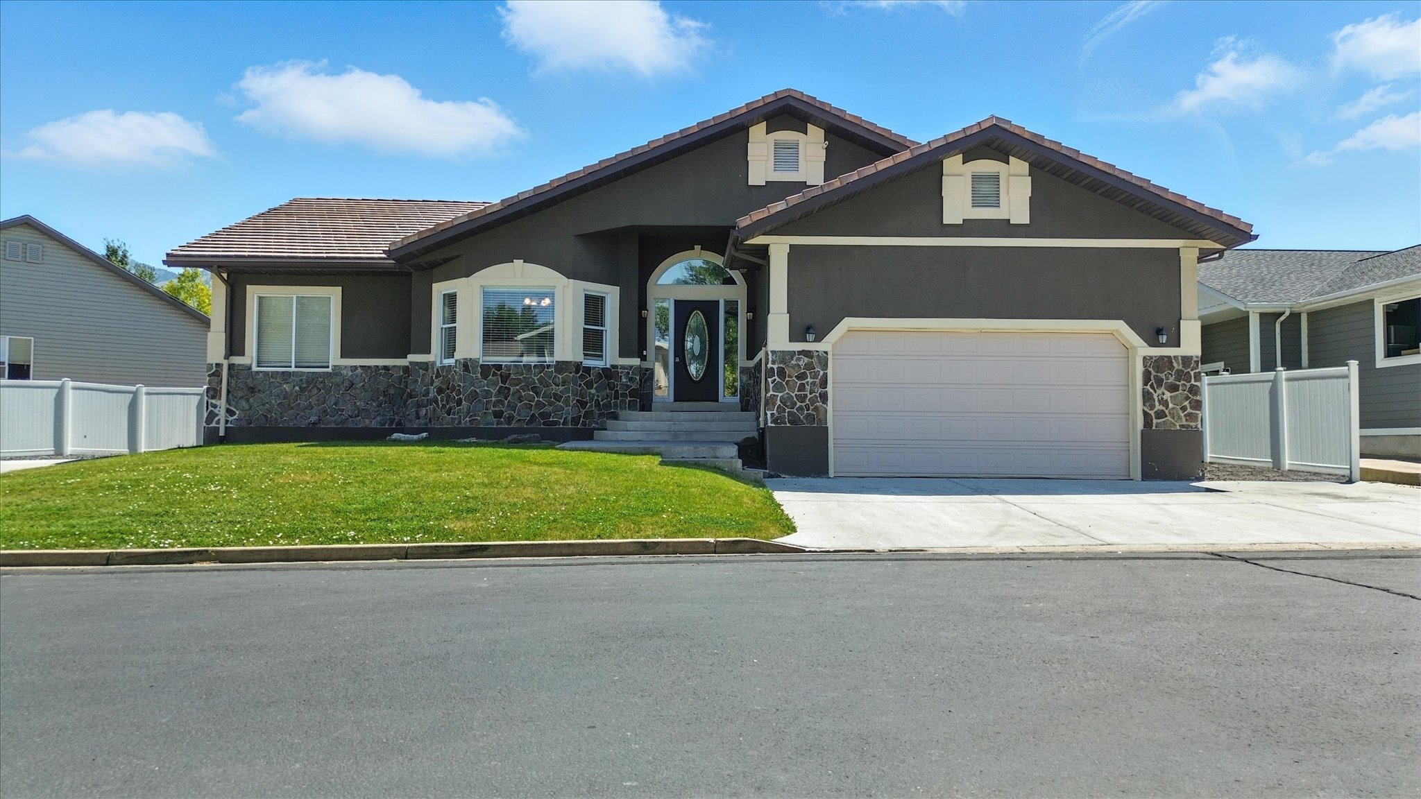 Ranch-style house with stone siding, a garage, concrete driveway, and stucco siding