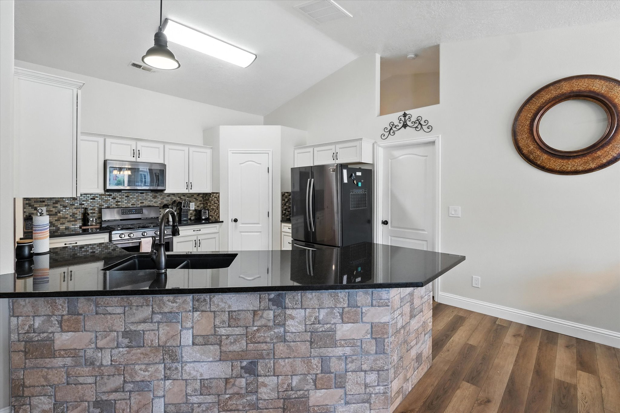 Kitchen with appliances with stainless steel finishes, dark countertops, vaulted ceiling, white cabinets, and decorative backsplash