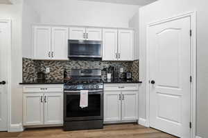 Kitchen with appliances with stainless steel finishes, dark countertops, decorative backsplash, light wood finished floors, and white cabinets