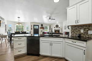 Kitchen with dishwashing machine, dark countertops, ceiling fan, a lit fireplace, and a peninsula