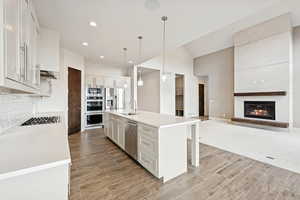 Kitchen featuring a center island with sink, pendant lighting, recessed lighting, a breakfast bar area, and light stone counters