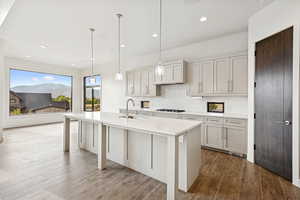 Kitchen with decorative backsplash, hanging light fixtures, recessed lighting, an island with sink, and dark wood-type flooring