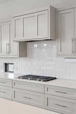 Kitchen with decorative backsplash, light stone countertops, stainless steel gas cooktop, and white cabinetry