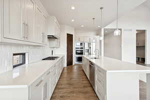 Kitchen with a kitchen island with sink, wood tiled floors, recessed lighting, white cabinets, and light stone counters