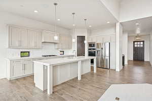 Kitchen with backsplash, hanging light fixtures, appliances with stainless steel finishes, a kitchen bar, and an island with sink