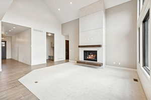Unfurnished living room with high vaulted ceiling, a fireplace, recessed lighting, and light wood-style floors