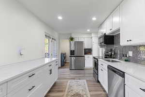 Kitchen with stainless steel appliances, white cabinets, light wood-type flooring, light stone counters, and recessed lighting